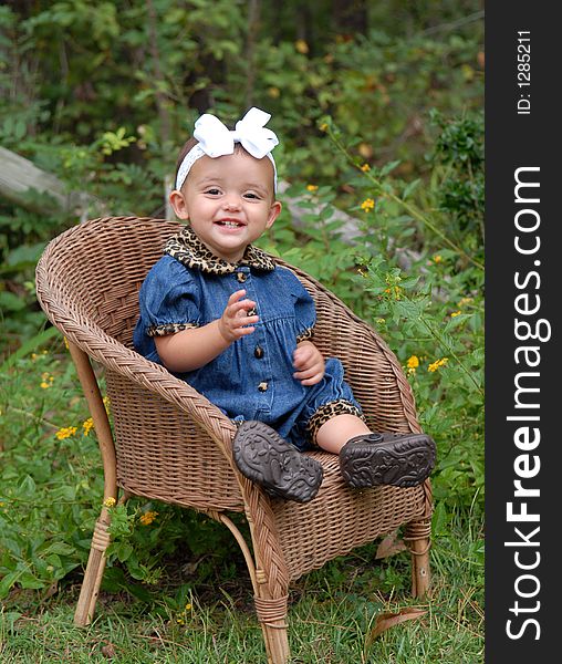 A darling baby girl sitting in a wicker chair wearing denim trimmed in leopard with a big bow in her hair outdoors. She's sooooo happy. A darling baby girl sitting in a wicker chair wearing denim trimmed in leopard with a big bow in her hair outdoors. She's sooooo happy