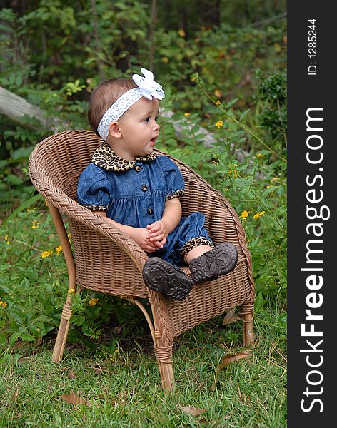 A darling baby girl sitting in a wicker chair wearing denim trimmed in leopard with a big bow in her hair outdoors. She's Looking away at something. A darling baby girl sitting in a wicker chair wearing denim trimmed in leopard with a big bow in her hair outdoors. She's Looking away at something.