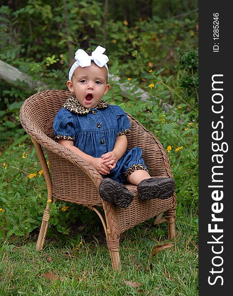 A darling baby girl sitting in a wicker chair wearing denim trimmed in leopard with a big bow in her hair outdoors. She's yawning so big - she must be really sleepy. A darling baby girl sitting in a wicker chair wearing denim trimmed in leopard with a big bow in her hair outdoors. She's yawning so big - she must be really sleepy