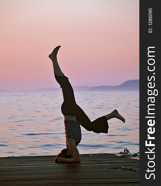 Young woman exercising yoga, balancing on the head, sea and sunset at the background. Young woman exercising yoga, balancing on the head, sea and sunset at the background