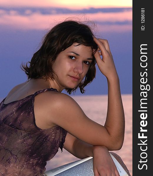 Young woman sitting at sunset, looking at camera  and smiling. Young woman sitting at sunset, looking at camera  and smiling