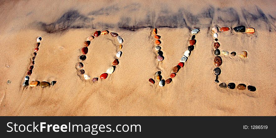 Word LOVE on beach sand, made from rocks