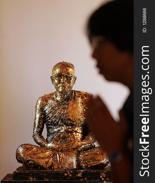 A Buddhist recites prayer near a Buddha statue in Thailand.