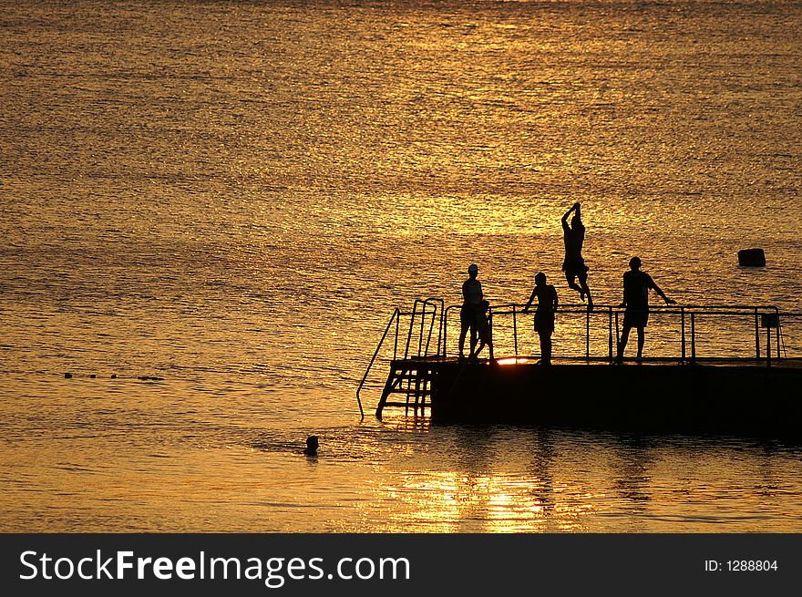 Silhouettes of people on a pier on a background of the orange sea. Silhouettes of people on a pier on a background of the orange sea