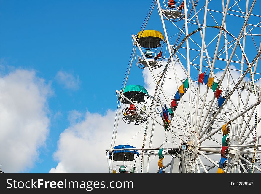 Part of a multi-coloured Ferris wheel on a background of the sky and clouds