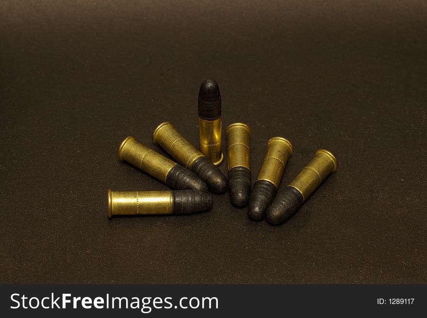 Seven .22lr cartridges in brass shells on black surface. Seven .22lr cartridges in brass shells on black surface