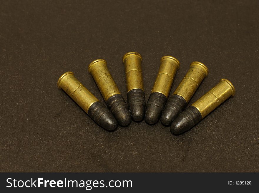 Six .22lr rimfire cartridges on black surface. Six .22lr rimfire cartridges on black surface