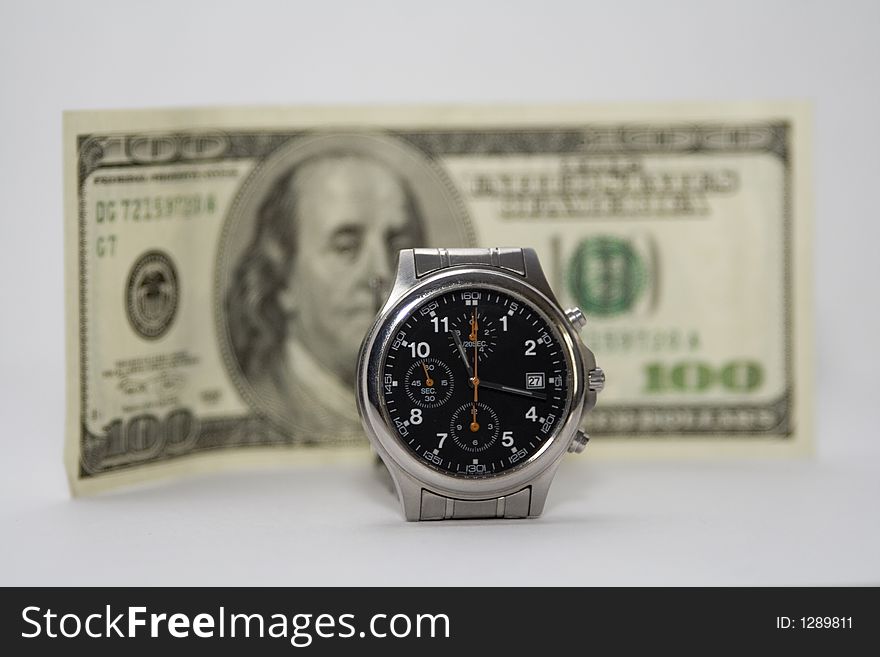 A wrist watch with the $100 bill in the background. Shallow depth of field, focus is on the watch. Time is money.