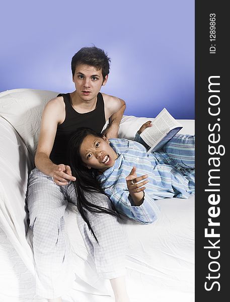 Couple on couch pointing finger at camera over blue background