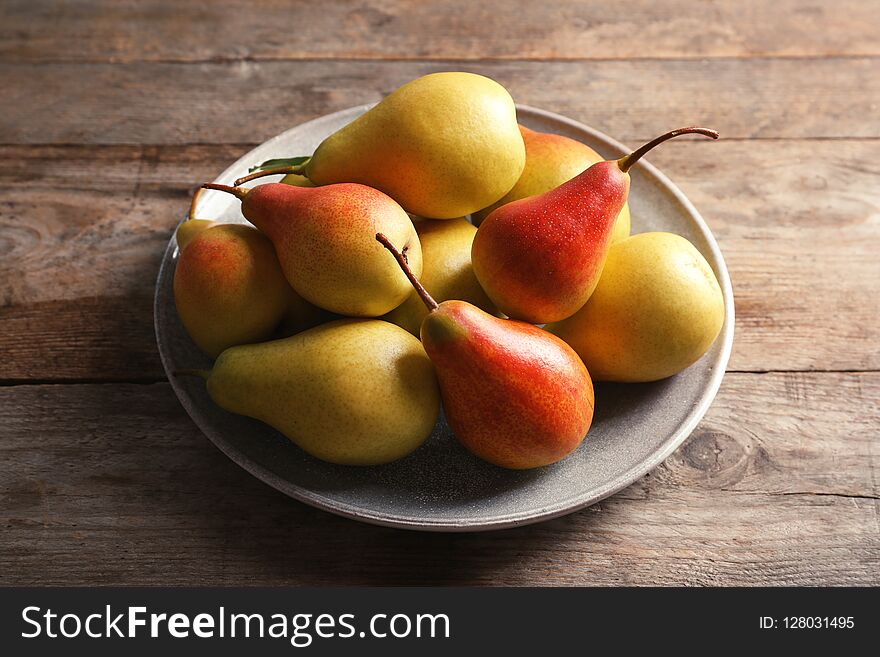 Plate with ripe pears on wooden background