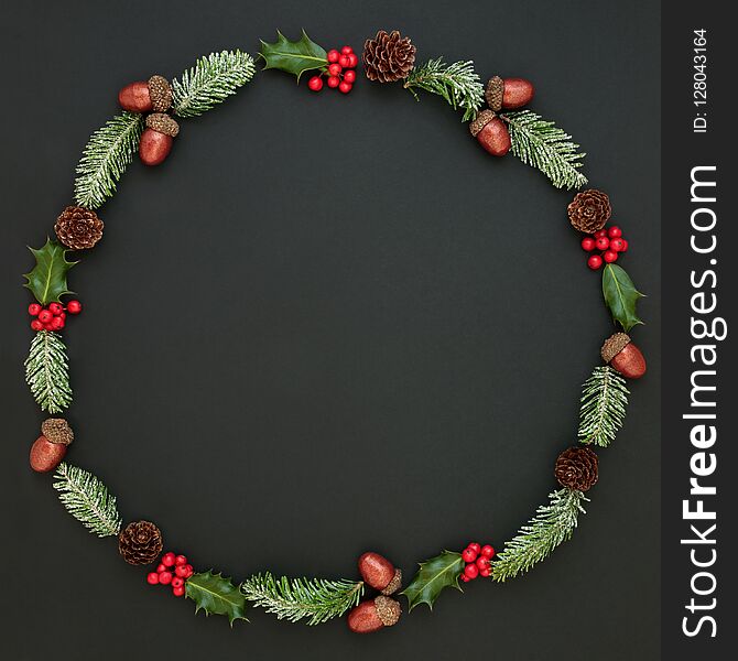 Natural winter and Christmas abstract wreath with snow covered fir, holly, ivy, mistletoe, acorns and pine cones on dark grey background. Traditional christmas greeting card for the festive season. Natural winter and Christmas abstract wreath with snow covered fir, holly, ivy, mistletoe, acorns and pine cones on dark grey background. Traditional christmas greeting card for the festive season.