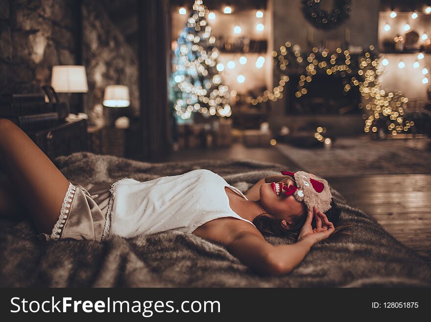 Young beautiful asian smiling woman is wearing pajamas lying in bed at home near christmas tree in cozy interior. Interior with christmas decorations. Young beautiful asian smiling woman is wearing pajamas lying in bed at home near christmas tree in cozy interior. Interior with christmas decorations.