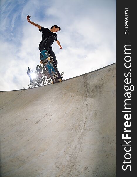 Skateboarder doing a tail slide on a croncrete pool at the skate park.