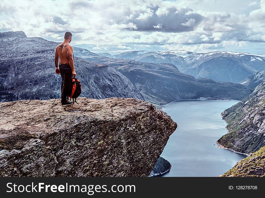 Tourist Man Standing In The Trolltunga And Enjoys A Beautiful View Of The Norwegian Fjord.