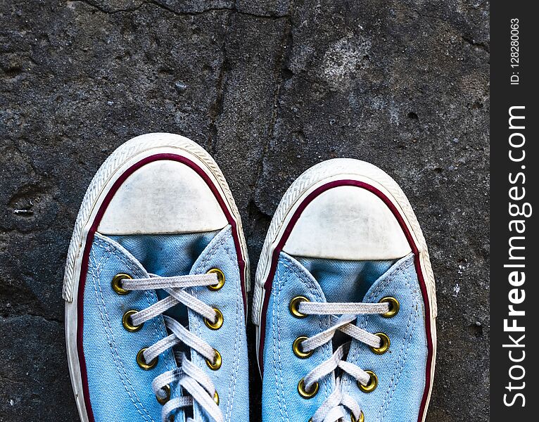 Pair of old worn blue textile sneakers on gray asphalt, top view