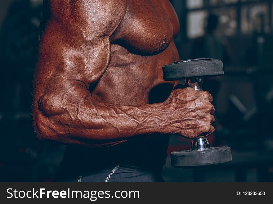 Man in gym. Muscular bodybuilder guy doing exercises with dumbbell. Strong person with Tense male hand with veins