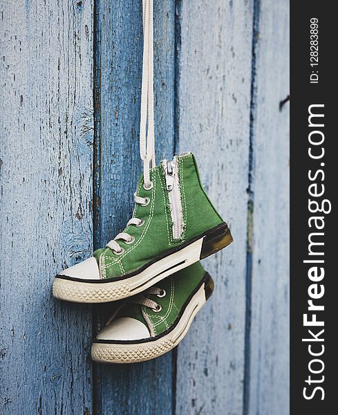 Pairs of old textile children`s green classic sneakers hang on a cord, blue shabby wooden background