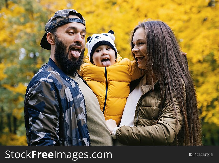 Happy family having fun outdoor. Close up portrait. Father, mother and daughter shows tongue. Autumn walk in the park