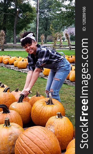 Teen girl picking up a pumpkin in a pumpkin patch