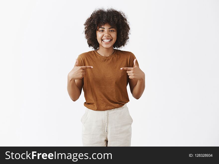 Studio shot of optimistic friendly african american girl with curly hair wanting being picked suggesting herself as candidate pointing at chest and smiling joyfully at camera with happy expression.
