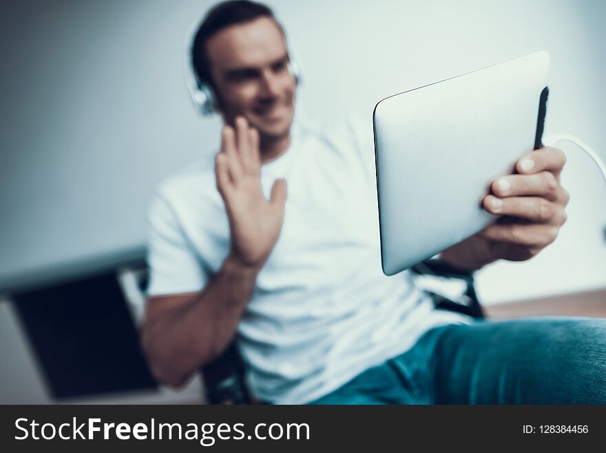 Blurred Disabled Man in Headphones Communicate Via Tablet. Smiling Person Wears T-Shirt and Blue Jeans Sits in Wheelchair Browsing Internet and Talking Via Video and Showing Hello Gesture. Blurred Disabled Man in Headphones Communicate Via Tablet. Smiling Person Wears T-Shirt and Blue Jeans Sits in Wheelchair Browsing Internet and Talking Via Video and Showing Hello Gesture.