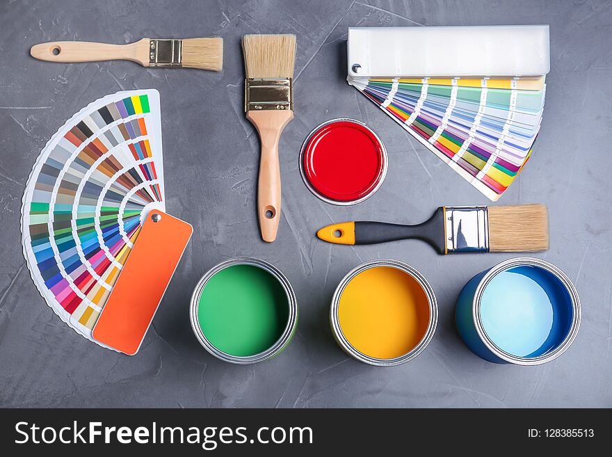 Flat lay composition with cans of paint, brushes and color palette samples on gray background