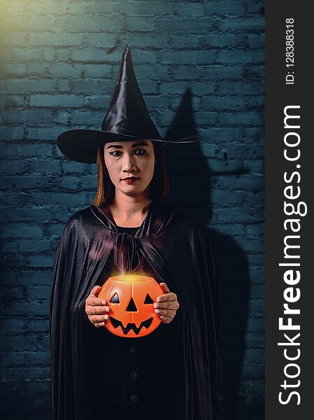 Portrait of woman in black Scary witch halloween costume holding halloween pumpkin with Old Brick Wall of the Ancient Castle of the Witch. Portrait of woman in black Scary witch halloween costume holding halloween pumpkin with Old Brick Wall of the Ancient Castle of the Witch