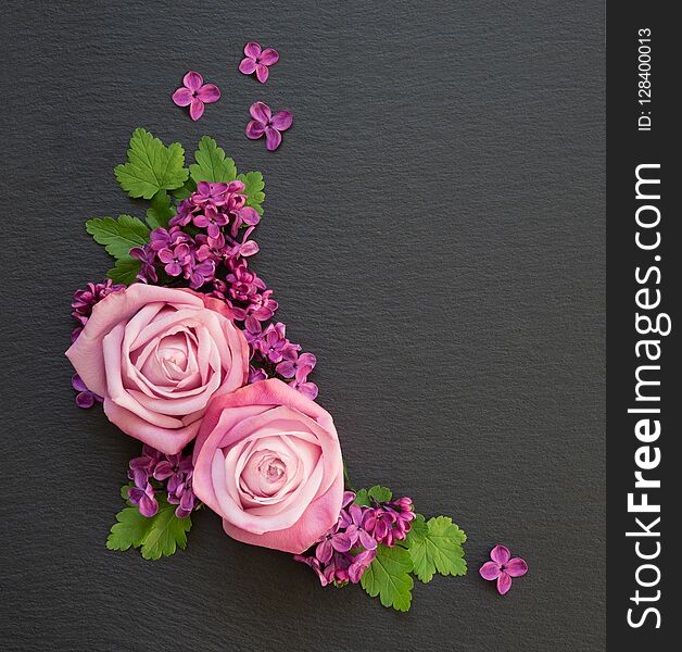 Decorative composition consisting of pink roses, violet lilac flowers and green leaves on a black slate with copy-space. Flat lay, top view, overhead view. Decorative composition consisting of pink roses, violet lilac flowers and green leaves on a black slate with copy-space. Flat lay, top view, overhead view