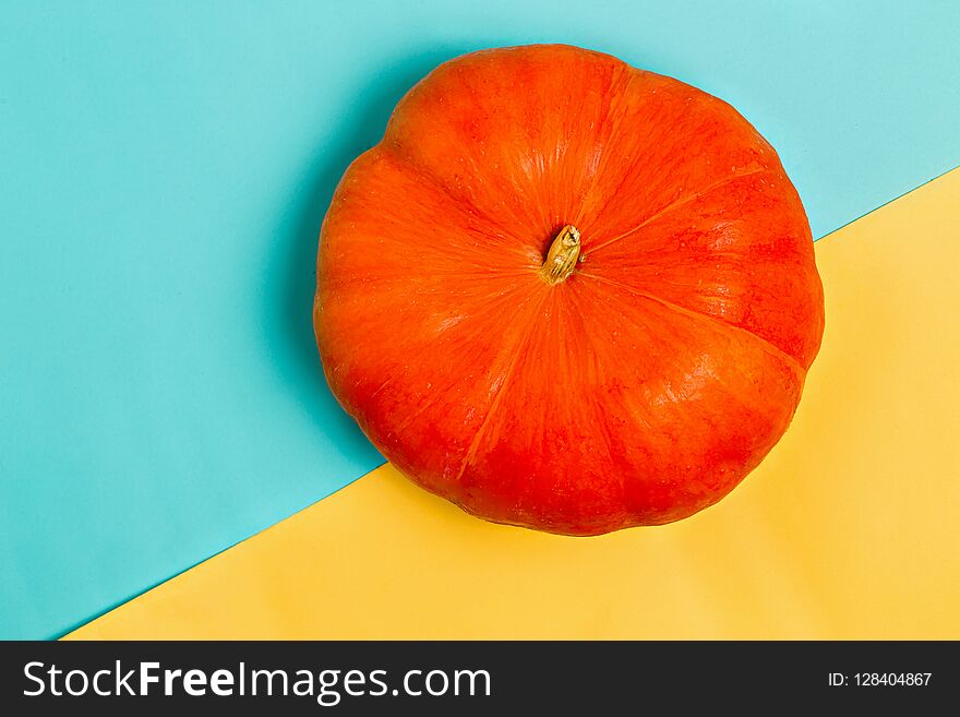 Beautiful orange pumpkin on colorful yellow and blue background, top view. Flat lay. Autumn, Halloween, harvest and holiday concept