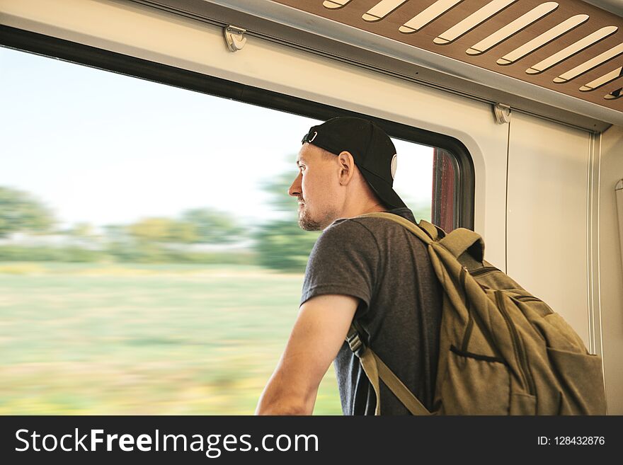 A young guy with a backpack inside the train looks out the window.