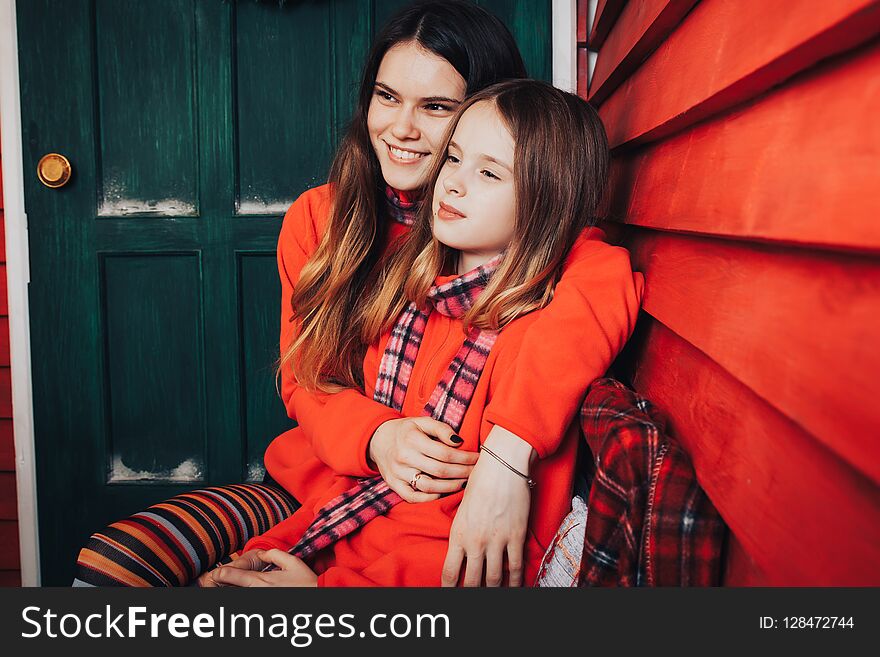 Two girls are sisters in red sweaters and striped scarves relax and have fun in the room, decorated for Christmas