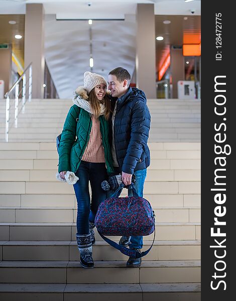 Couple of the travellers in warm clothes in the steps at the room of station