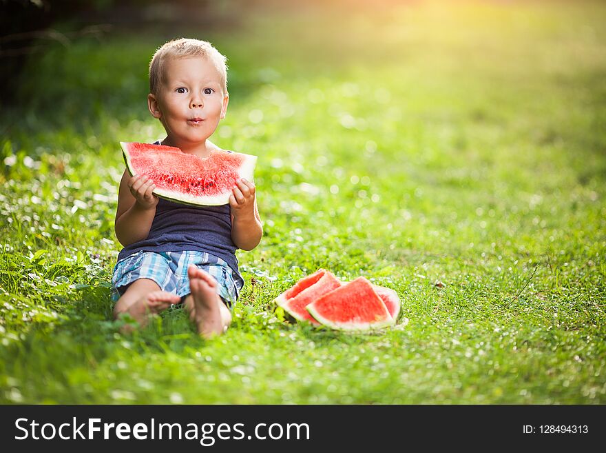 Cute toddler sitting outdoords and eating a slice of watermelon. Cute toddler sitting outdoords and eating a slice of watermelon