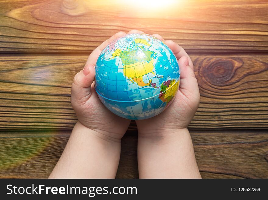 Globe in hands in the sun on a wooden background