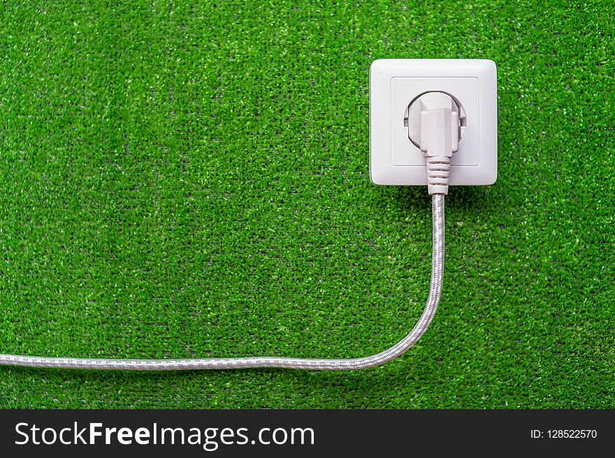 Concept of ecological reception of an electricity. Electric socket and plug with a cord on a background of green grass