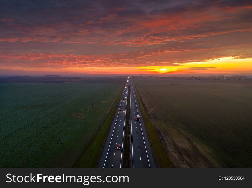 Road with cars under dramatic red sky in the morning. Transportation background. Aerial landscape. Autumn industrial morning.