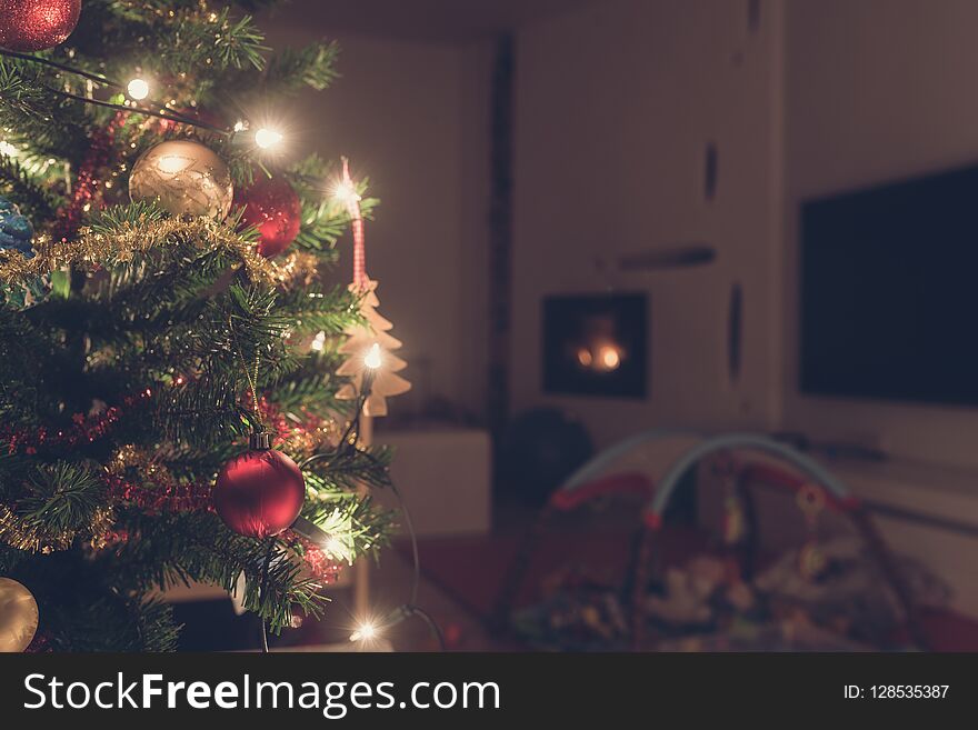 Retro image of decorated Christmas tree with lights indoors in living room with fire place and baby playground.