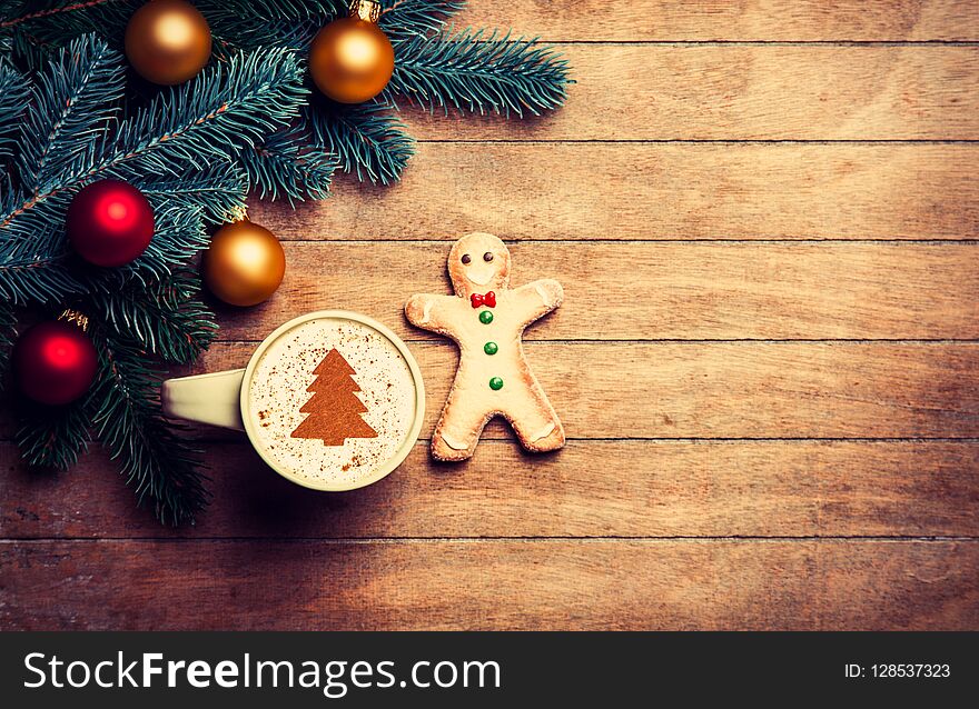 Cappuccino with gingerbread man and pine branch on wooden table.