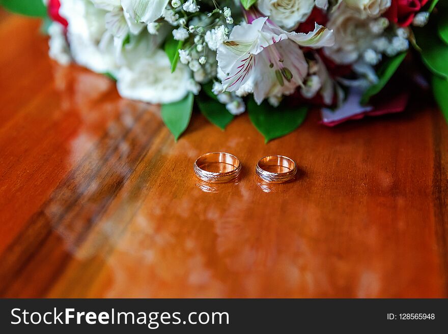 Beautiful wedding rings lie on wooden surface against background of bouquet of flowers. Declaration of love, spring. Wedding card, Valentine's Day greeting. Wedding rings. Wedding day details