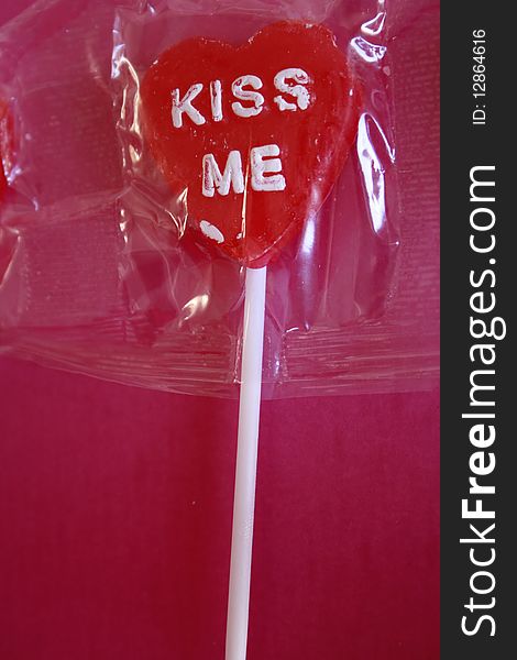 Lollipop shaped as a red heart with kiss me printed on it in white. Lollipop shaped as a red heart with kiss me printed on it in white