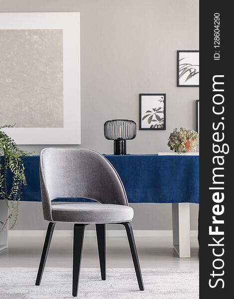 Modern chair at table with blue cloth in grey dining room interior with posters and lam