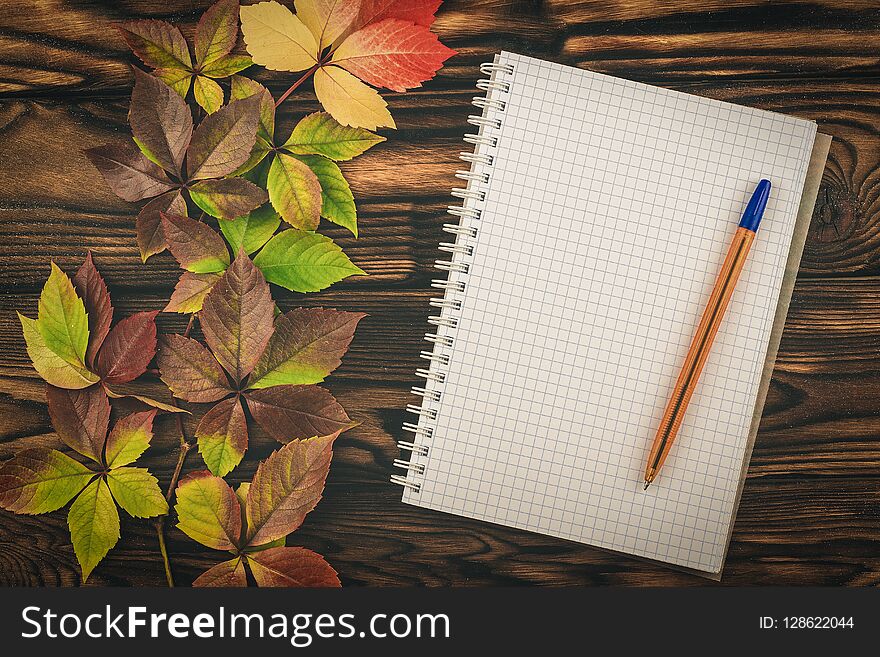 Notepad and pen with autumn leaves on a wooden table. Letter.