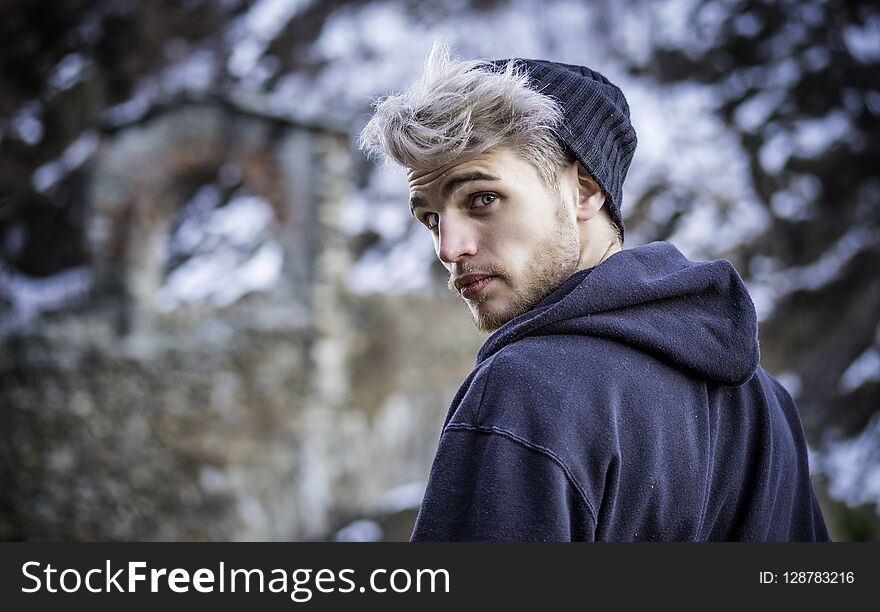 Portrait of young man in hoodie posing outdoor in winter setting with snow all around, looking at camera. Portrait of young man in hoodie posing outdoor in winter setting with snow all around, looking at camera.