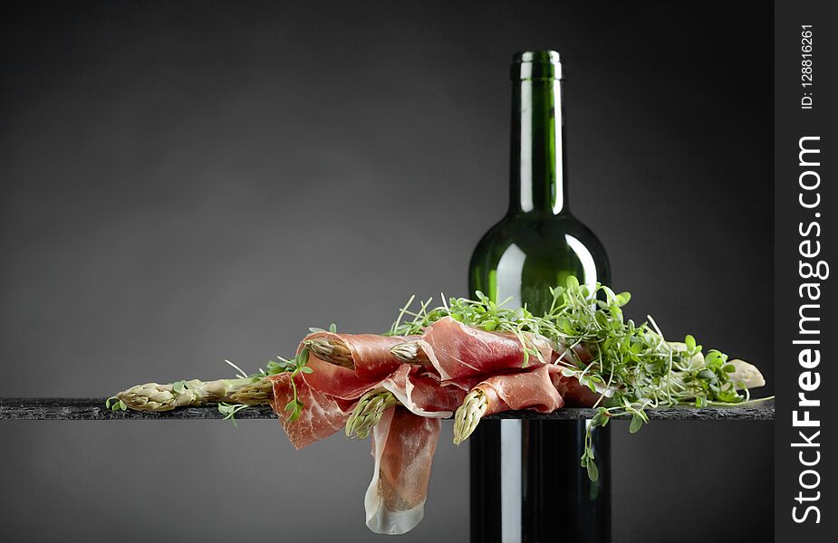 Asparagus wrapped in prosciutto with red wine on a dark background. Asparagus wrapped in prosciutto with red wine on a dark background.