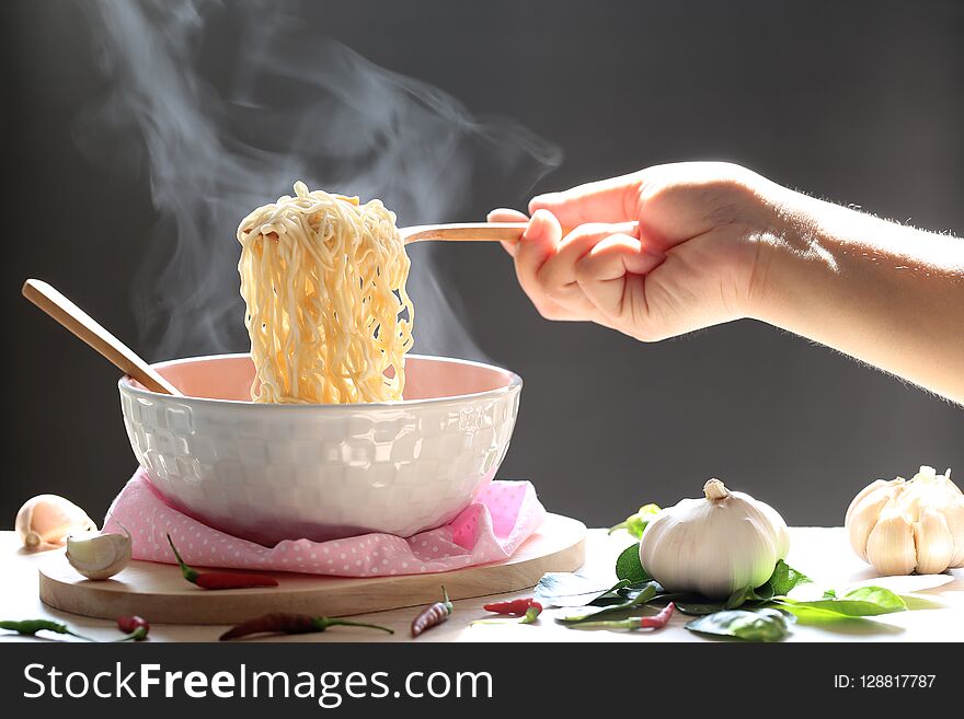 Woman Hand Holding Fork Of Instant Noodles In Cup With Smoke Rising And Garlic On Dark Background, Sodium Diet High Risk Kidney F