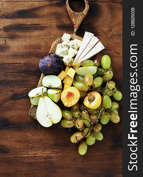 Top view flat lay appetizers table Various snacks: grapes, peach, apricot, pear, apples, hard cheese, brie cheese and roquefort cheese on wooden table. Top view flat lay appetizers table Various snacks: grapes, peach, apricot, pear, apples, hard cheese, brie cheese and roquefort cheese on wooden table