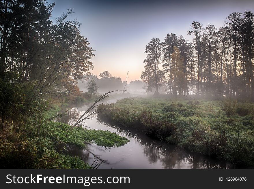 River in the fog, just before sunrise. A warm glow in the clouds from the first rays of the sun.