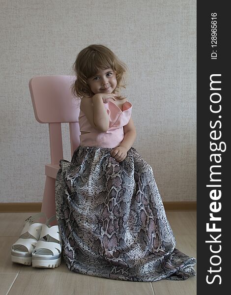 Little funny girl sitting in a chair in her mother`s big dress