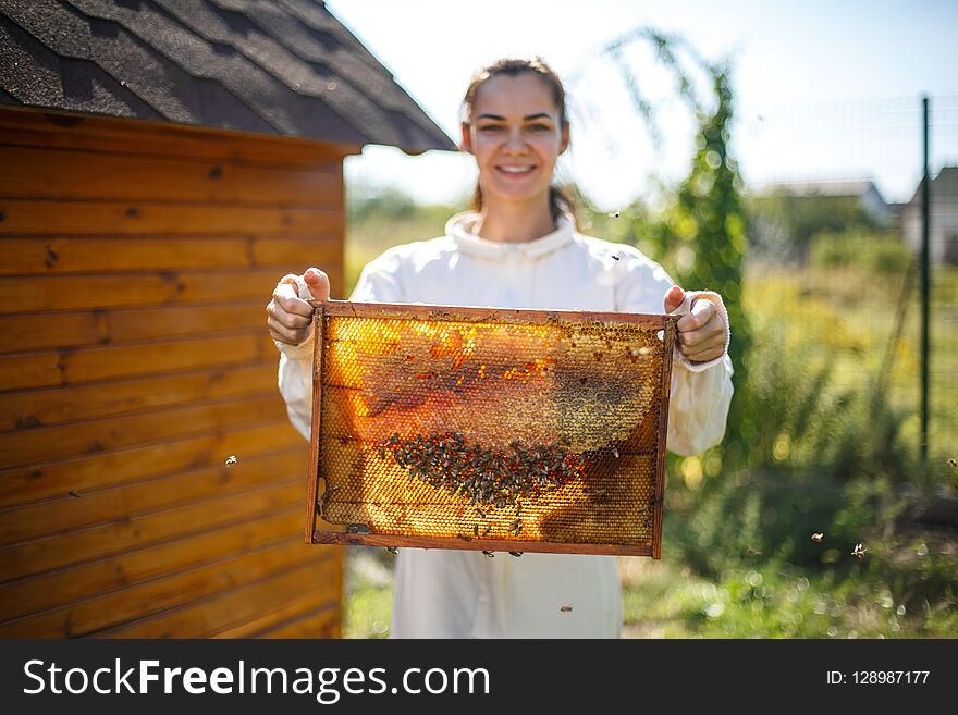 Young female beekeeper hold wooden frame with honeycomb. Collect honey. Beekeeping concept