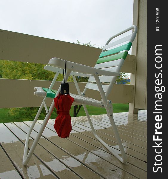 A picture of  an umbrella hanging on a rained soaked chair on a rain soaked porch. The person sitting there has gone inside. A picture of  an umbrella hanging on a rained soaked chair on a rain soaked porch. The person sitting there has gone inside.